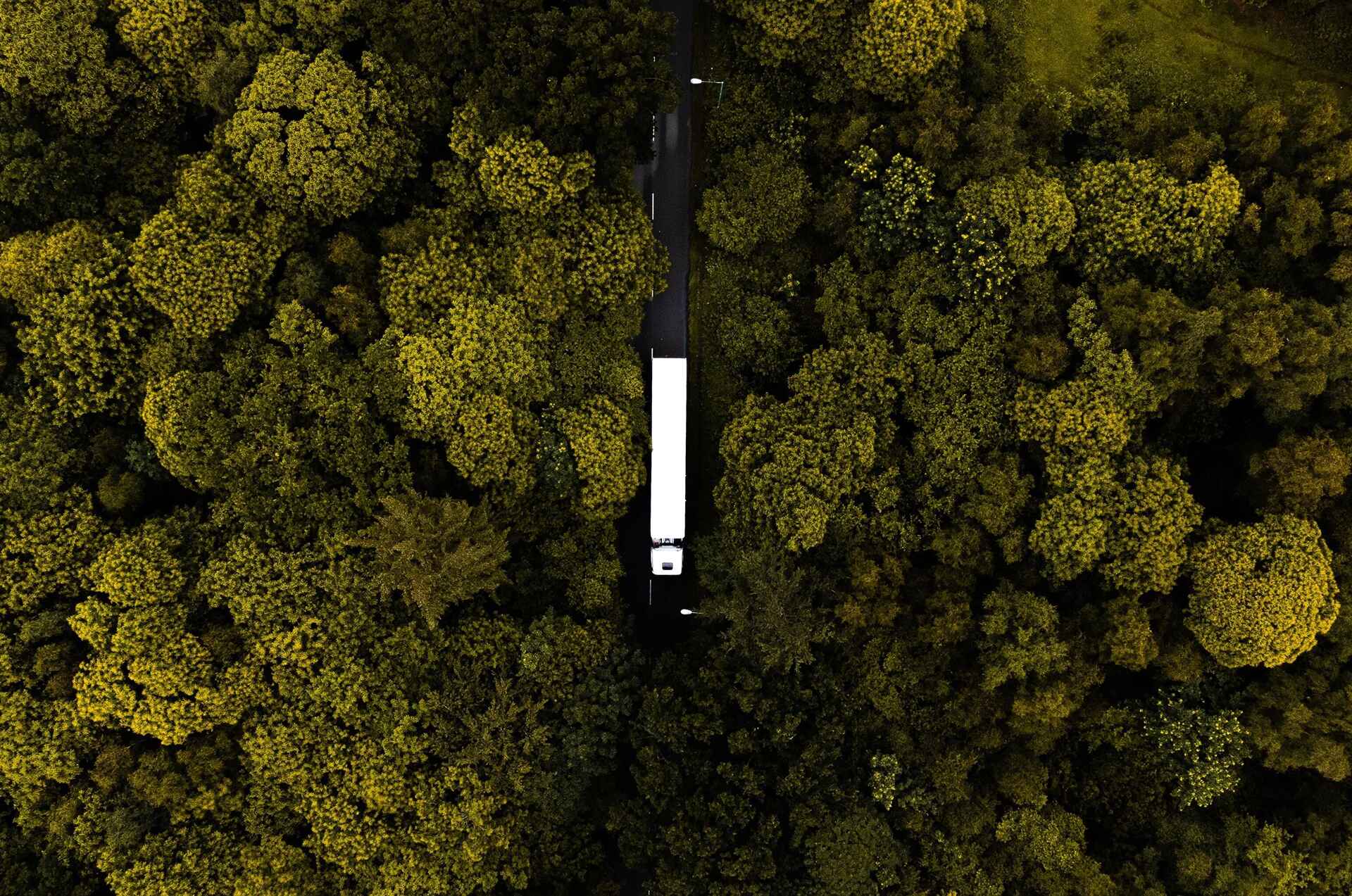drone image of a white semi truck driving down a road lined by wooded areas