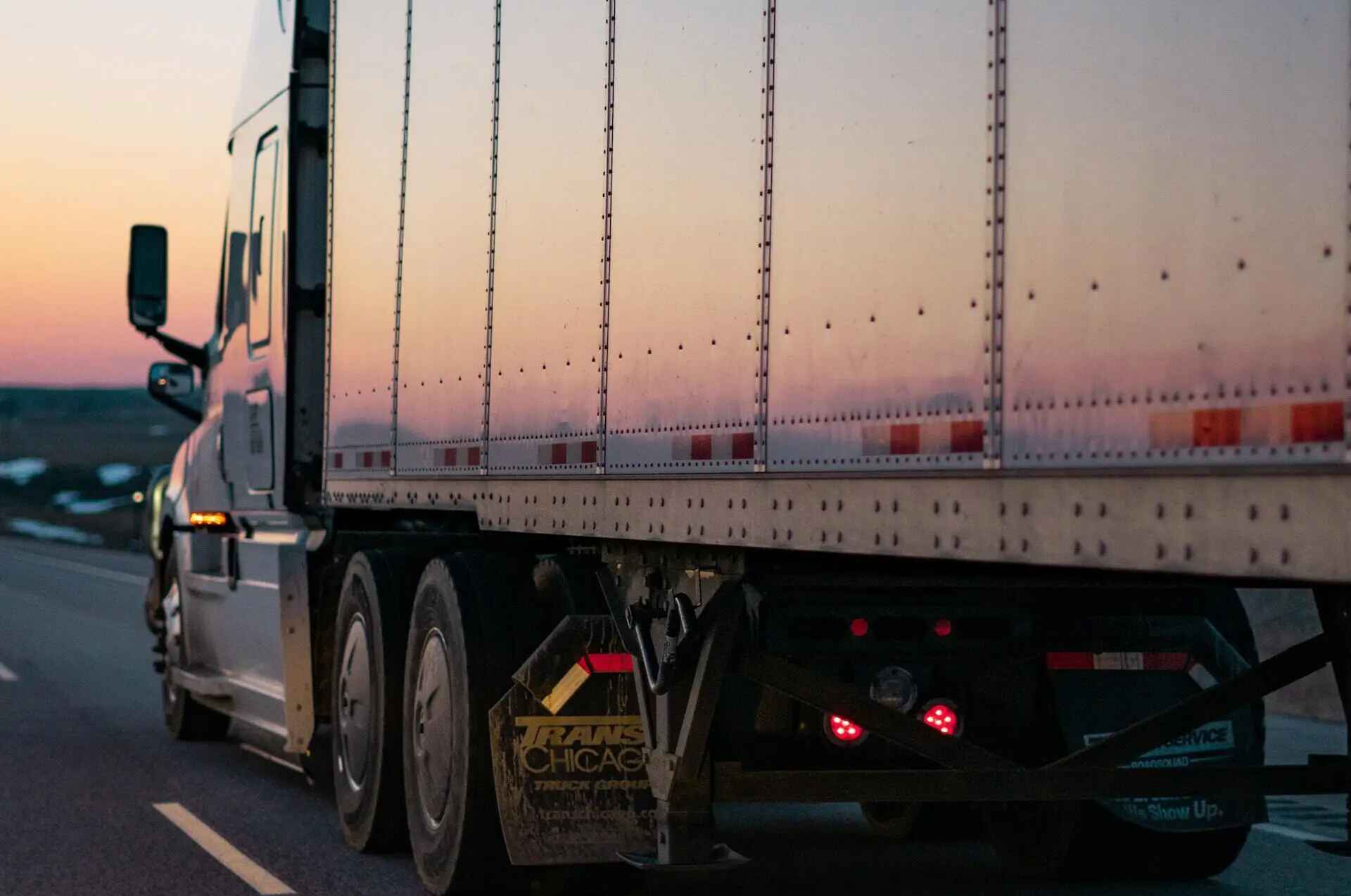 Close up image of the side of a semi truck driving down a highway at sunset
